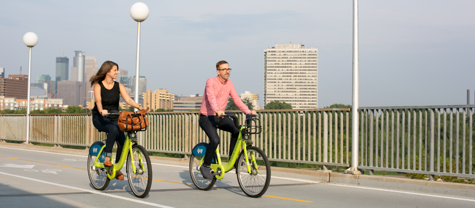 two people on bikes on a bridge with downtown in the background