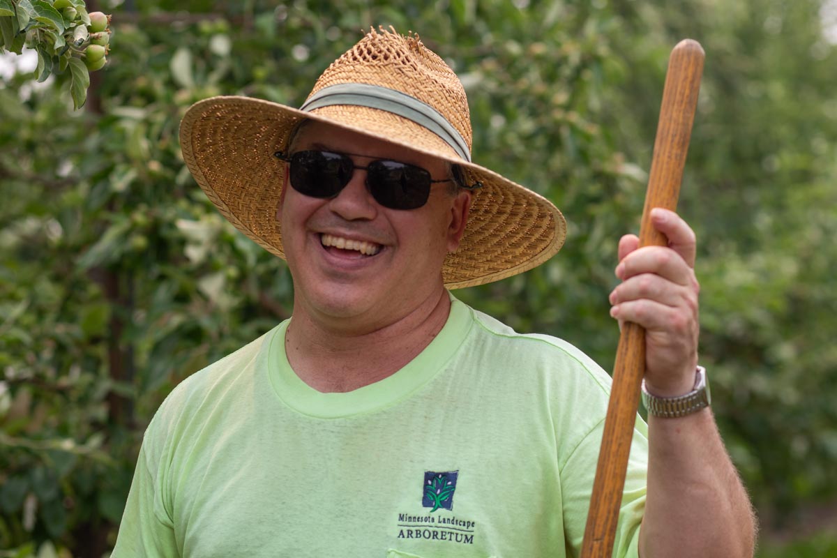 John Mazzarella in sunglasses and a straw hat holding a hoe