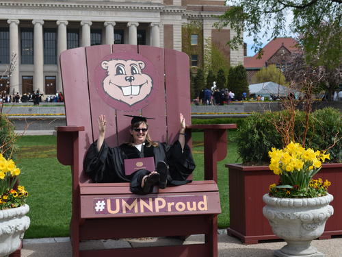 Lisa K. sitting on the Goldy Gopher giant Adirondack chair in front of Coffman Memorial Union