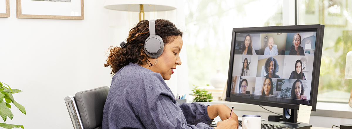 A person wearing headphones sits in front of a computer screen showing several people on a video conference.