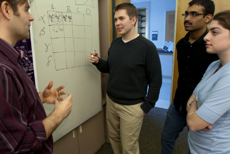 A person presenting information on a whiteboard to a small group of people.