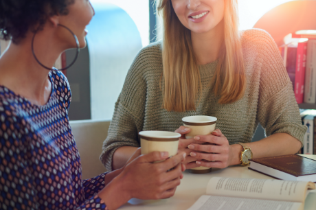 Two women having a discussion while sitting at a table drinking coffee.