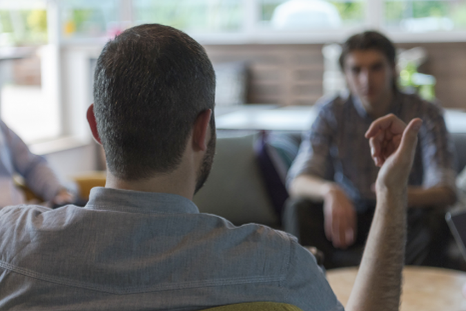 Three people sitting in chairs around a coffee table having a discussion.